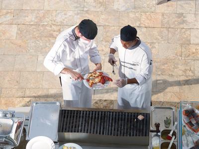 Dos chefs con ropa blanca preparan carne a la parrilla en una cocina de hotel.