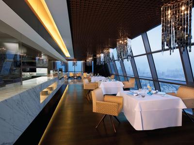 Restaurante elegante con ventanas panorámicas, manteles blancos e iluminación moderna en un hotel.