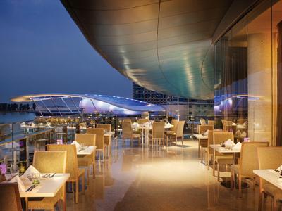 Área exterior moderna de restaurante con mesas y sillas al atardecer junto al agua.