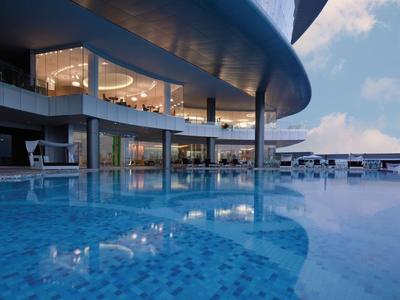 Área de piscina moderna con grandes ventanas de vidrio y techo curvado al atardecer.