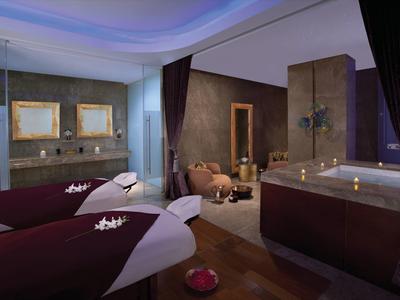 Área de spa elegante con camillas de masaje y jacuzzi iluminado en tonos apagados.