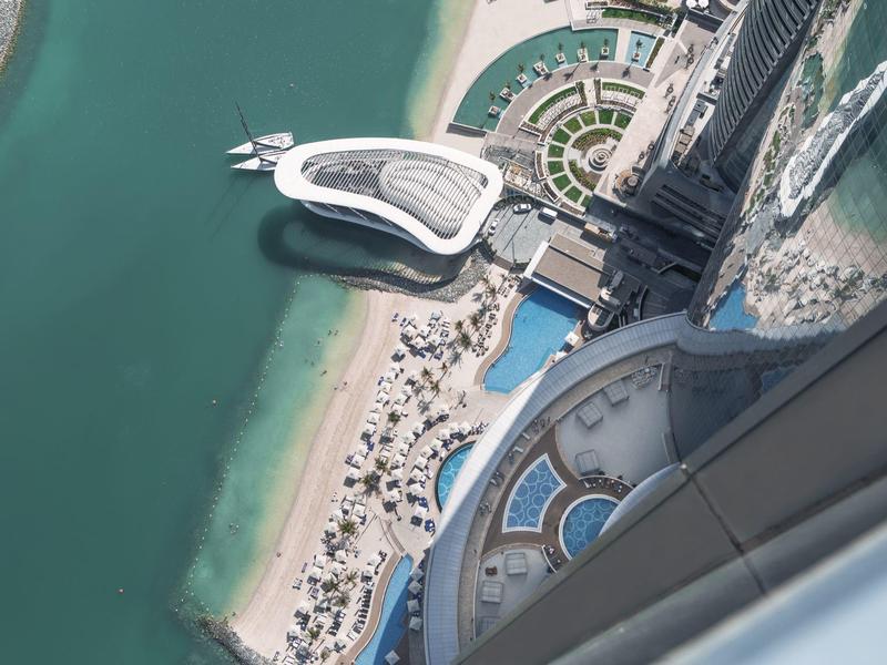 Vista desde gran altura de piscina, playa y hotel moderno junto al mar turquesa.