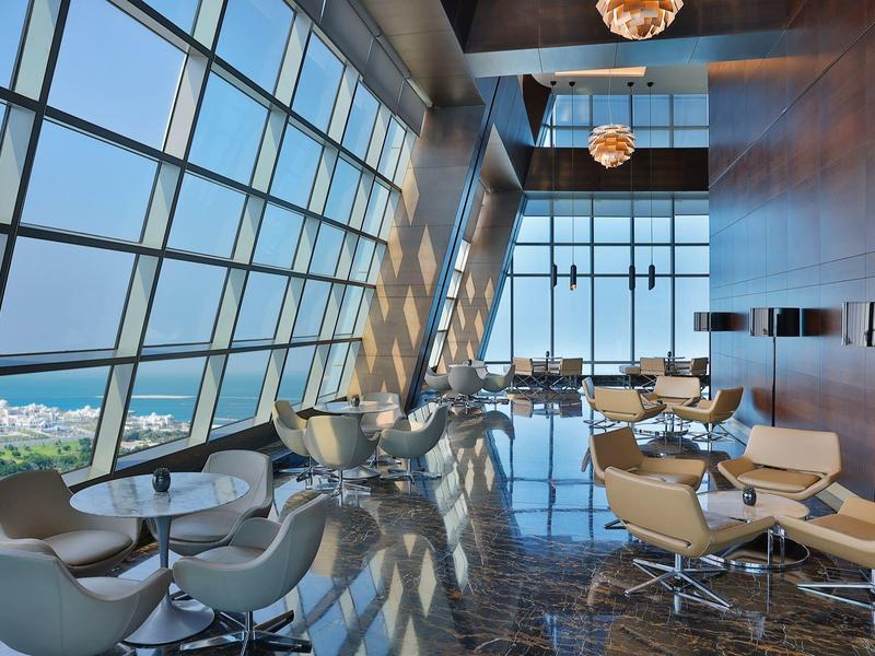 Lounge de hotel moderna con grandes ventanas y vista al mar a la luz del día.