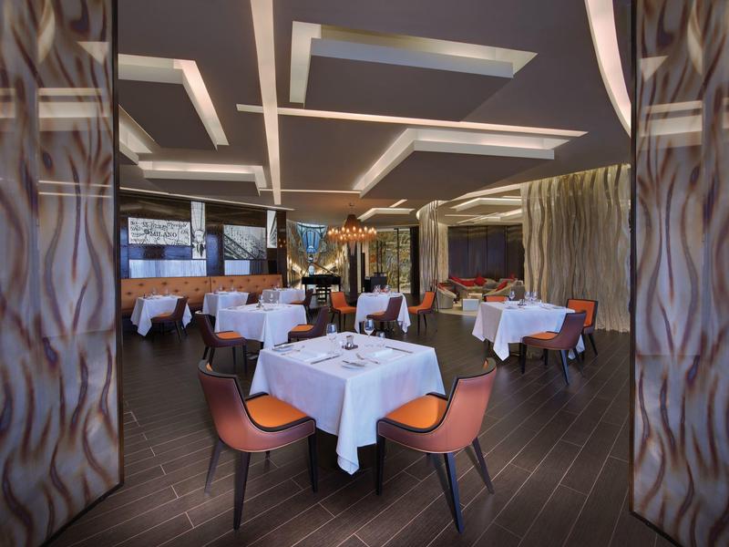 Habitación de hotel luminosa con cama grande, sofá y ventanas de piso a techo con vistas al mar.