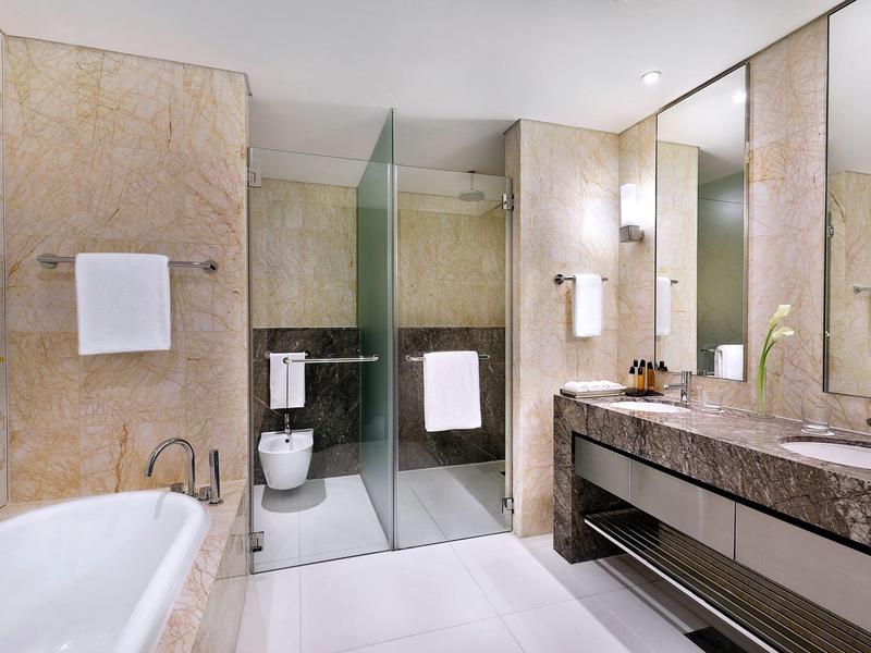 Baño de hotel elegante con bañera independiente, ducha de vidrio y amplio lavabo.