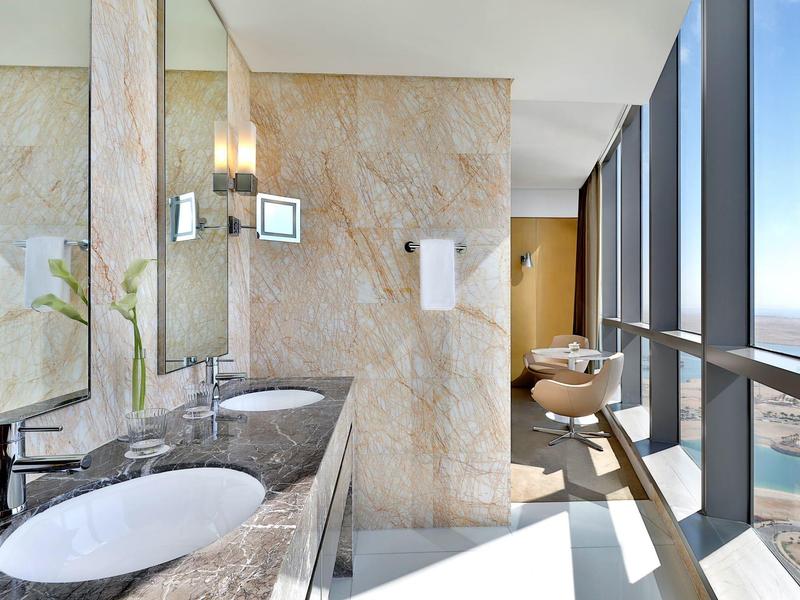 Baño luminoso con grandes ventanas, dos lavabos y vista al mar.