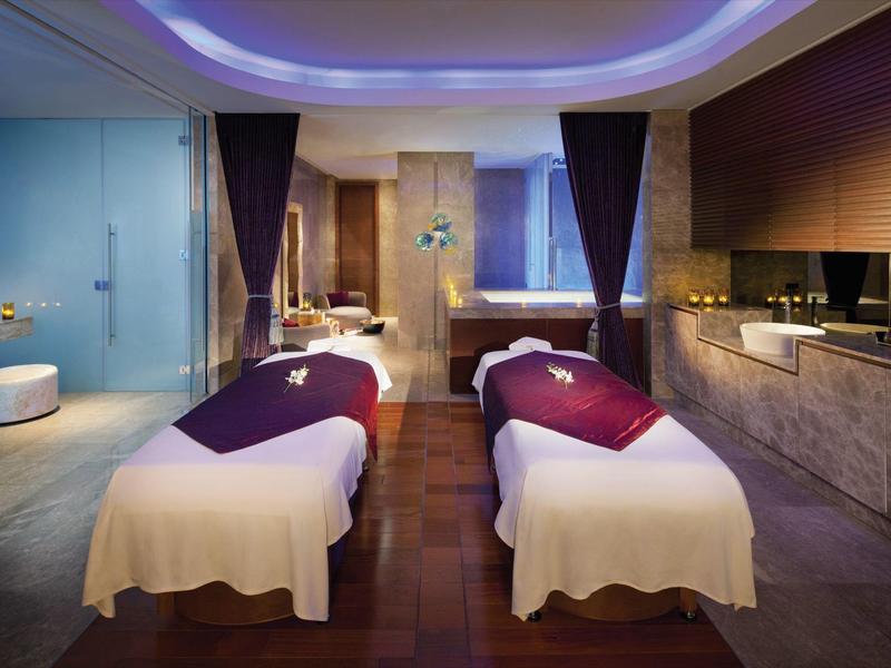 Sala de spa lujosa con dos camillas, luz tenue y equipamiento moderno.