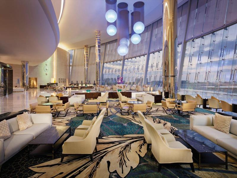 Amplia zona de vestíbulo de hotel con grupos de asientos modernos en colores neutros y grandes ventanales.