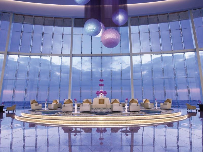 Amplio vestíbulo moderno con recepción circular y grandes ventanales con vistas al cielo y al mar.