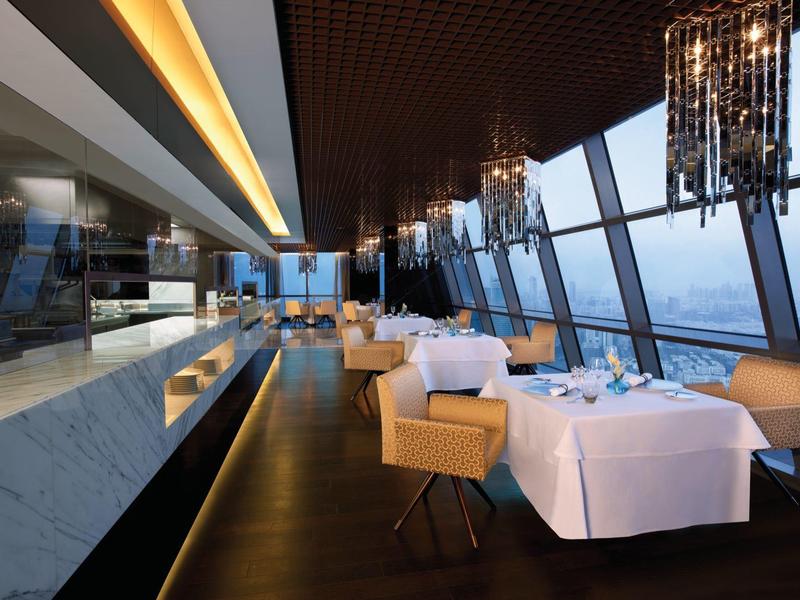 Restaurante elegante con ventanas panorámicas, manteles blancos e iluminación moderna en un hotel.