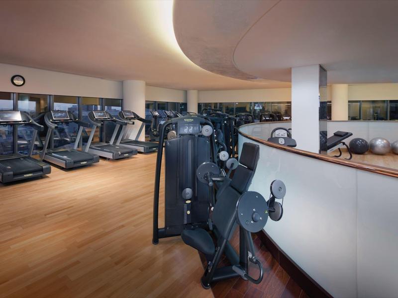 Gimnasio moderno con cintas de correr, máquinas de fuerza y grandes ventanas con vista exterior.