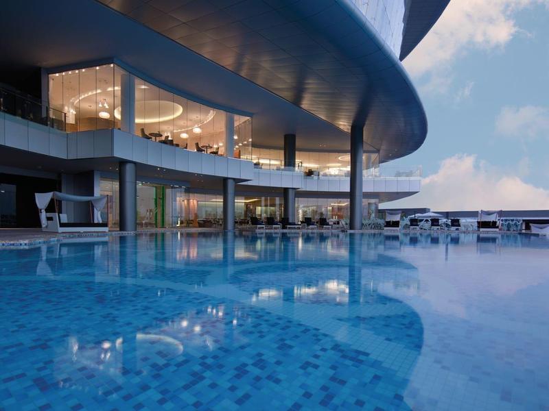 Área de piscina moderna con grandes ventanas de vidrio y techo curvado al atardecer.