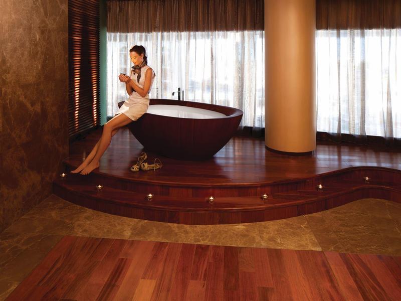 Mujer relajándose con bebida en plataforma de madera junto a bañera independiente en baño lujoso.