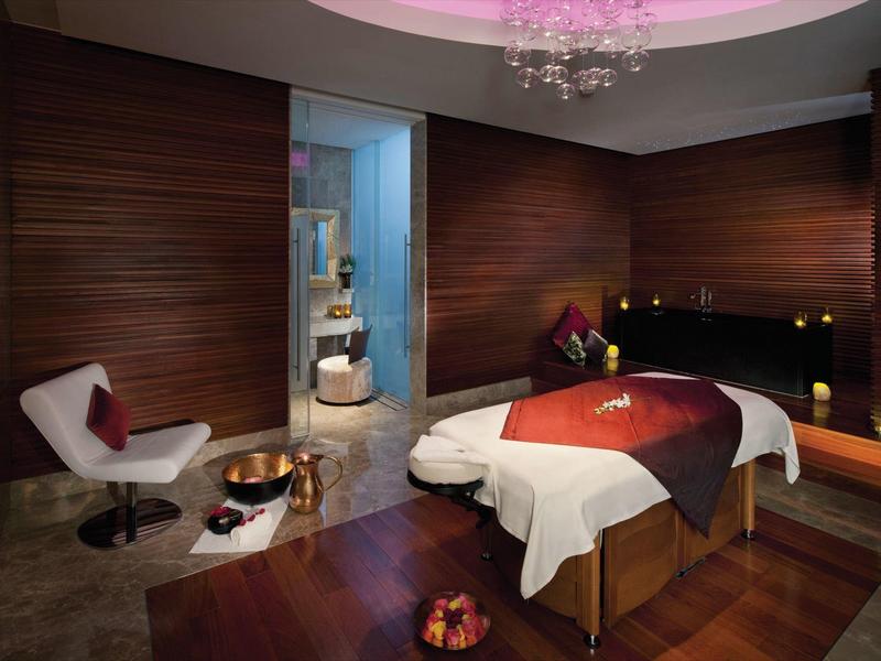 Elegante sala de spa con camilla de masaje, decoración cálida de madera y iluminación suave para relajación en hotel.