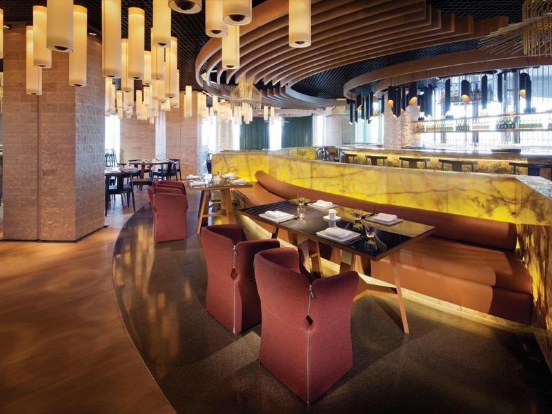 Restaurante moderno con sillas rojas, iluminación colgante y barra amarilla en diseño elegante.