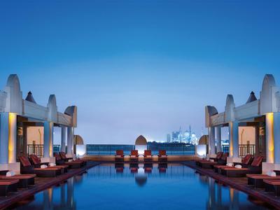 Luxusní bazén s výhledem na moře, obklopený moderními lehátky a kabinami při západu slunce.