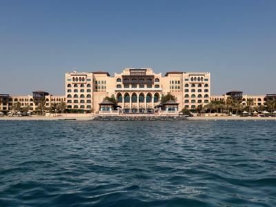 Gran hotel de lujo frente al mar con cielo despejado y agua tranquila en primer plano.