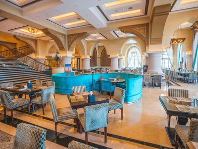 Área elegante del lobby del hotel con sofás azules, sillones y techos decorativos en tonos cálidos beige y azul.