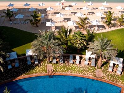 Widok na basen hotelowy z palmami i leżakami na plaży nad błękitnym morzem.