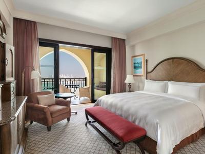 Elegancki pokój hotelowy z podwójnym łóżkiem, częścią wypoczynkową i balkonem z widokiem na morze.