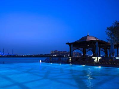 Piscina exterior iluminada con pabellón y crepúsculo azul claro junto al agua