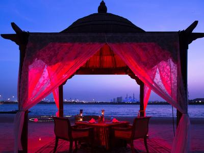 Romantická večeře pod pavilonem u vody s městskými světly v pozadí.