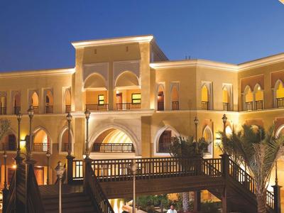 Osvětlená budova hotelu se schody, bazénem a palmovou výzdobou v noci.