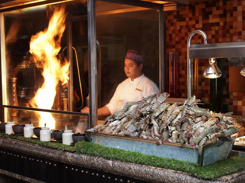 Cocinero prepara mariscos a la parrilla con fuego abierto en un restaurante.