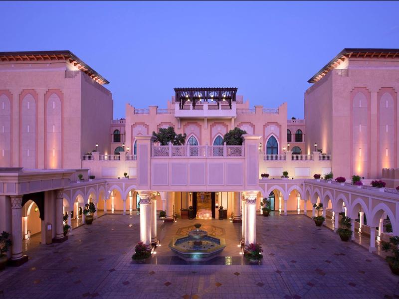 Vista nocturna de un hotel con arquitectura árabe y luces cálidas iluminando el patio central