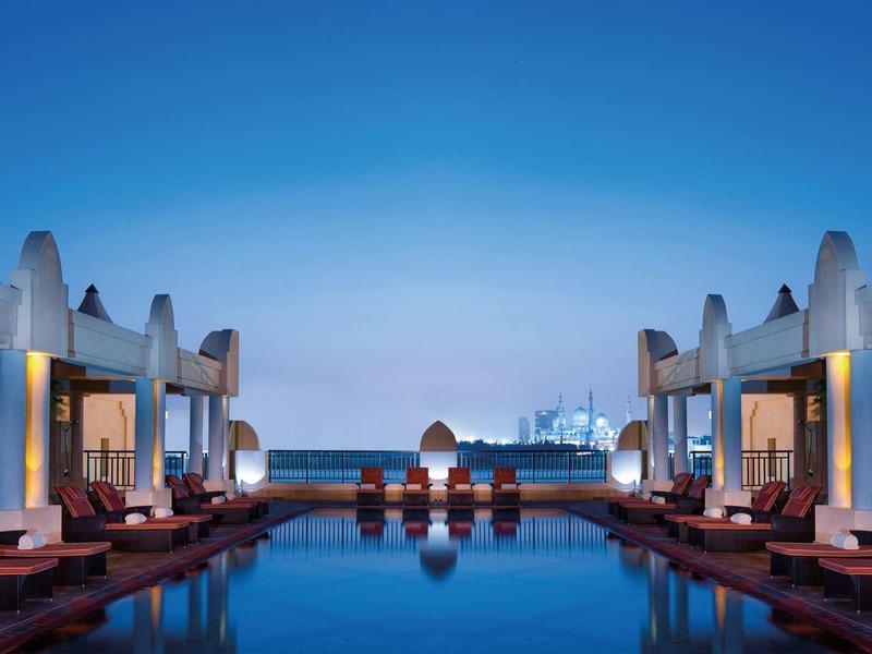 Piscina simétrica con áreas de descanso acogedoras en un hotel moderno al atardecer.