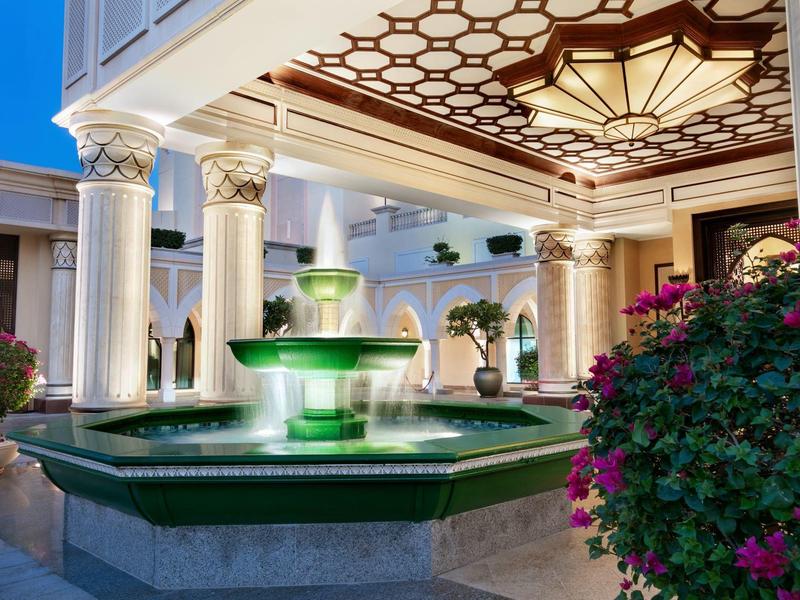 Elegante entrada del hotel con fuente iluminada y columnas decorativas de noche.