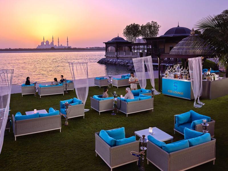 Muebles de salón modernos con cojines azules en la playa al atardecer con mezquita al fondo.