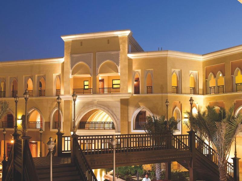 Hotel iluminado con arco, escaleras y agua en el patio interior de noche.