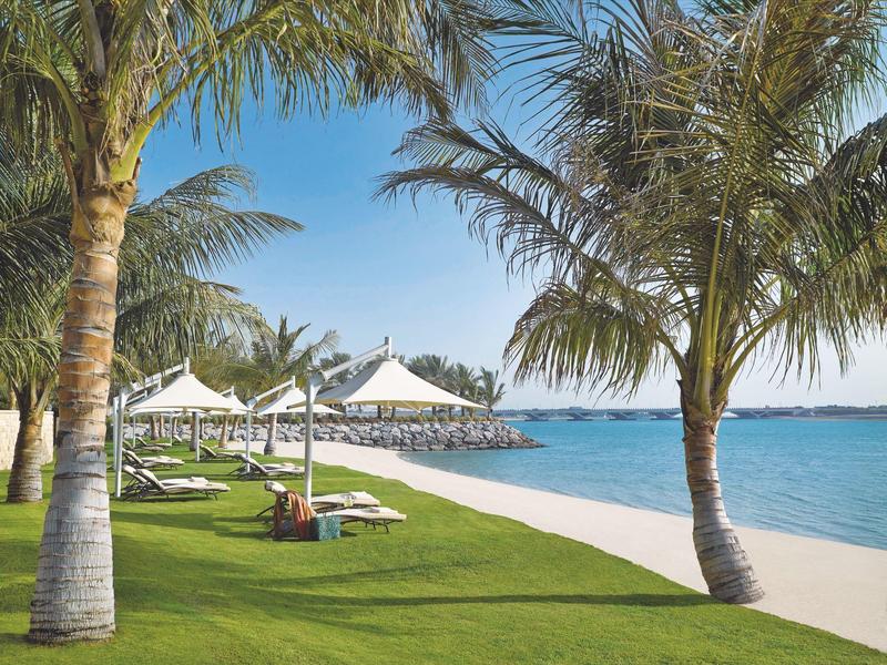 Playa con palmeras, hamacas bajo sombrillas blancas y mar azul bajo un cielo despejado.