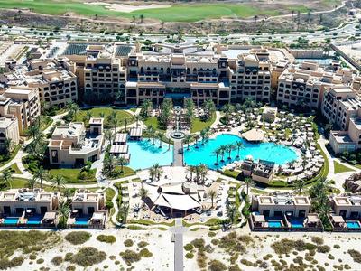 Großes Strandhotel mit mehreren Gebäuden, geschwungenem Pool und Palmen im Sandgebiet.