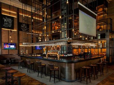 Moderne Hotelbar mit Holzhockern, warmem Licht und industriellem Design.