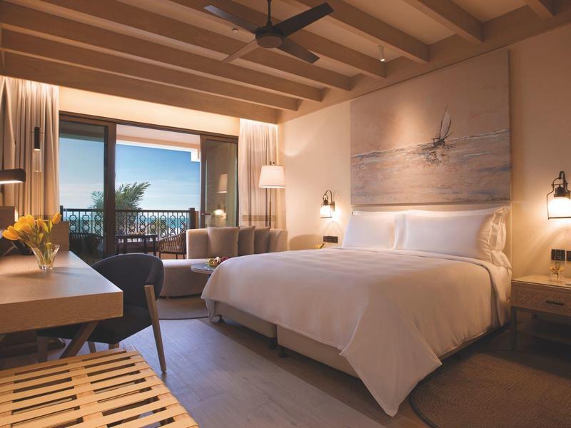 Modern hotel room with large bed and sea view through the window.