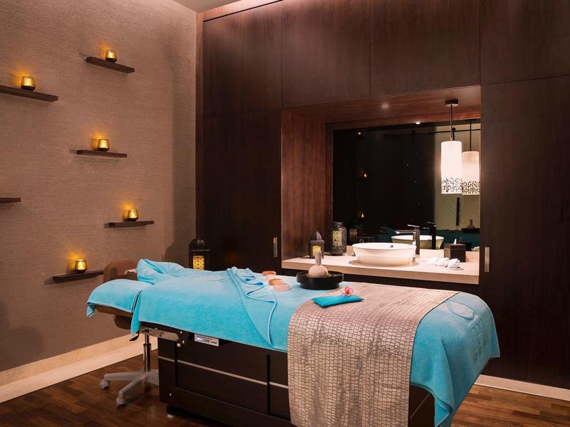 Cozy wellness room with massage table, soft lighting, and burning candles on the wall.