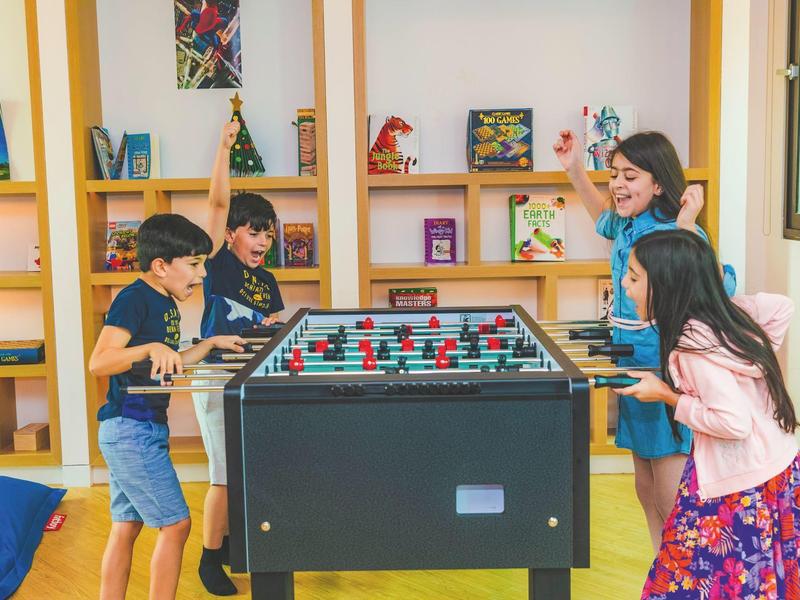 Four kids enthusiastically play foosball in a bright, cozy room.