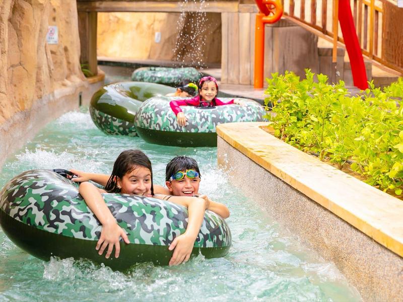 Children ride green tubes down a water channel in a water park.