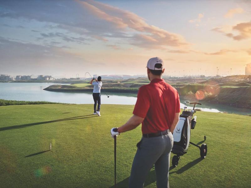 Two golfers on a well-maintained golf course with lake and sunset in the background.