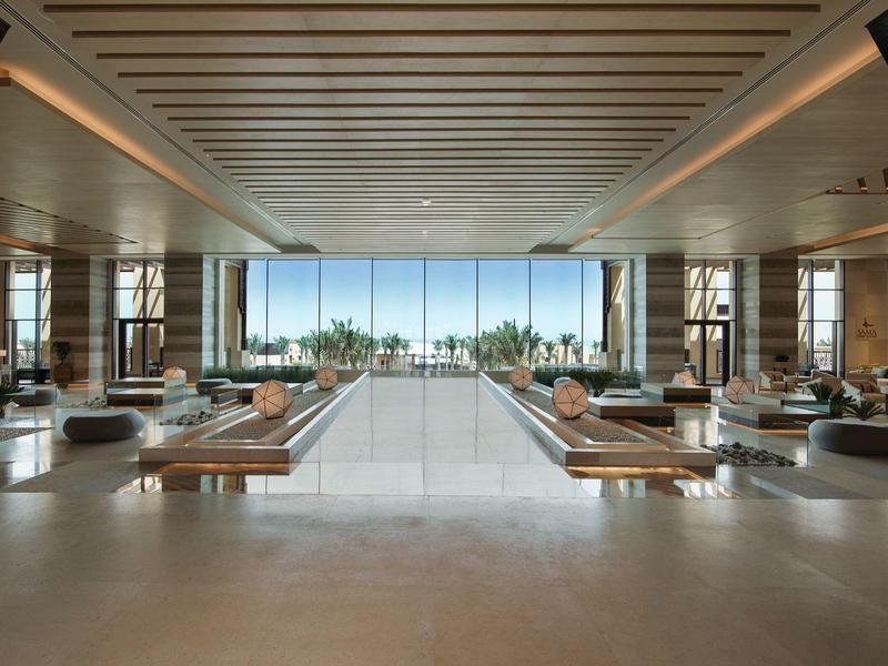 Spacious modern lounge area with wooden lamps and view of palm trees and sea.