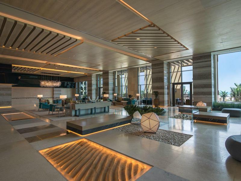 Modern hotel lobby with wooden slatted ceiling and large windows overlooking outdoor greenery.