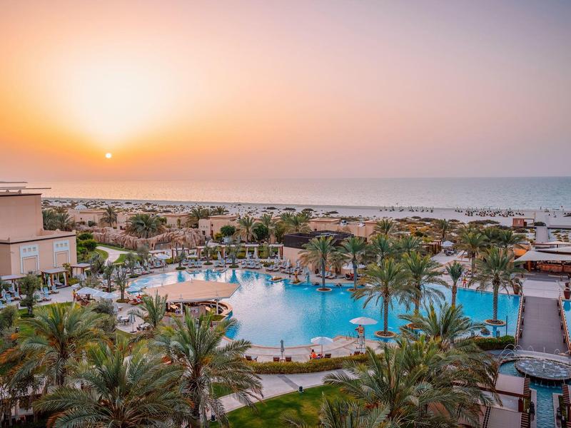 Hotel resort with large pool surrounded by palm trees at sunset by the sea