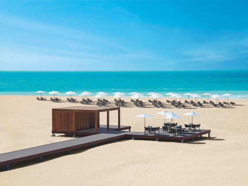 Empty beach with a row of sunshades and seating area in the foreground.