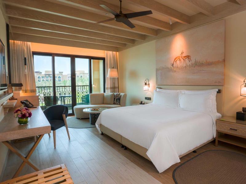 Modern hotel room with large bed, desk, balcony, and city view