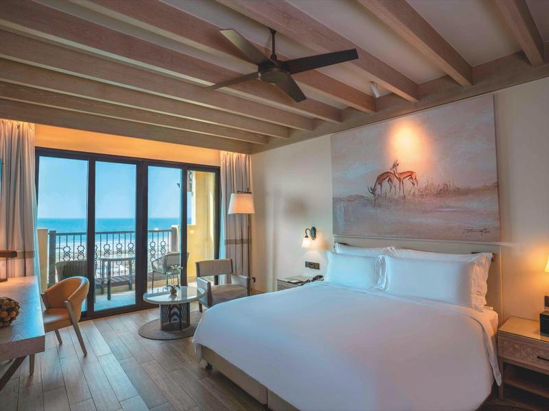 Modern hotel room with large bed, balcony, and sea view.