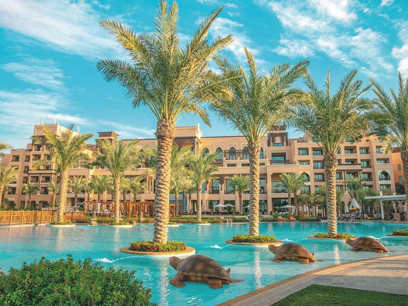 Luxury resort with large pool, palm trees, and calm atmosphere under a blue sky.