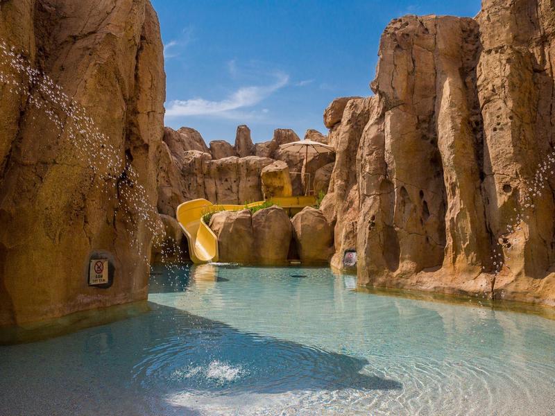 A clear water pool surrounded by tall rocks and a yellow water slide.