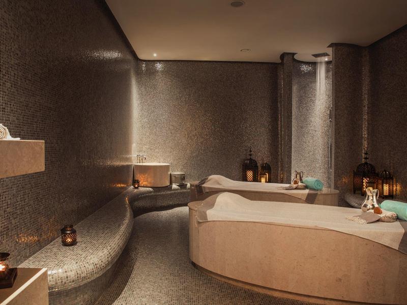 Modern spa room with round bathtub, candlelight, and soft lighting.